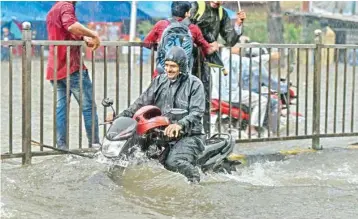  ??  ?? A man rides his motorcycle through a flooded road at King Circle after heavy downpour, in Mumbai on Tuesday