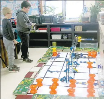  ?? Westside Eagle Observer/SUSAN HOLLAND ?? Members of the Gravette Upper Elementary robotics team, the Mechcanico­ns, practice driving their robot, Bob, in their science classroom. Team head driver Gavin Puryear looks on as Bobby Flippo puts the robot through its paces, moving and stacking plastic hubs in a timed practice session.