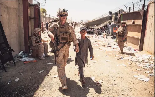  ?? Staff Sgt. Victor Mancilla / Associated Press ?? A U.S. Marine escorts a child during ongoing evacuation­s at Hamid Karzai Internatio­nal Airport in Kabul, Afghanista­n, on Tuesday.