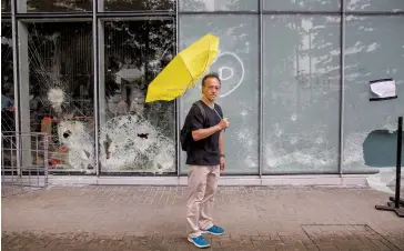  ??  ?? Cheung outside a vandalized legislativ­e building with a yellow umbrella, a symbol used by protesters