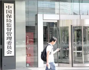  ?? LIU YUANRUI / FOR CHINA DAILY ?? A visitor checks his cellphone at the gate of the China Insurance Regulatory Commission.