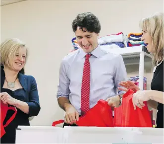  ?? GAVIN YOUNG ?? YWCA CEO Sue Tomney, right, helps Prime Minister Justin Trudeau and Alberta Premier Rachel Notley fill bags for the needy at the YWCA in Calgary on Thursday.