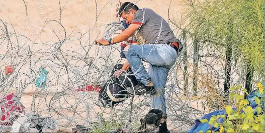  ?? ?? MIND THE GAPS: Asylum-seeking migrants go through concertina-wire fence Thursday after crossing the Rio Grande into the US from Mexico.