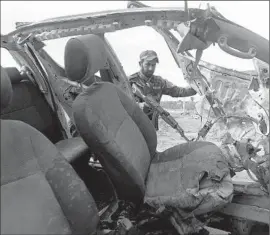  ?? Ahmad al-Rubaye Agence France-Presse ?? NEAR FALLOUJA, a Shiite fighter supporting the Iraqi government against Islamic State inspects a burned vehicle in February said to belong to the militants.