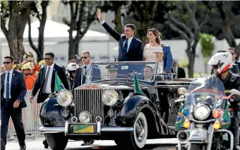 ?? AP ?? Flanked by first lady Michelle Bolsonaro, Brazil’s President Jair Bolsonaro waves as he rides in an open car after his swearing-in ceremony, in Brasilia.