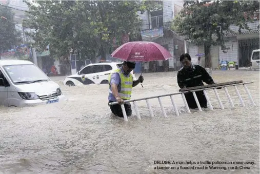  ??  ?? DELUGE: Aman helps a traffic policeman move away a barrier on a flooded road inWanrong, north China