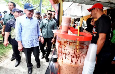  ?? — Bernama photo ?? Anwar drops by a drinks stall during a walkabout of the 2024 MAIWP Carnival site.