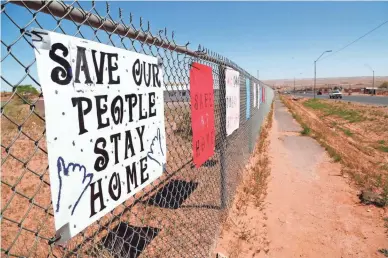  ??  ?? Signs on a fence in Tuba City in April remind residents to shelter in place to fight against the spread of the coronaviru­s. The Navajo Reservatio­n has seen a spike in COVID-19 cases.