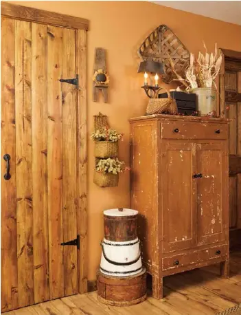  ??  ?? Left: Old hardware adds vintage character to a newly built door in the master bedroom. Next to it, a white bucket stacked with other rustic containers provides contrast to the room’s darker wood tones and highlights the chippy finish of the primitive wardrobe cabinet.Below: Allie and Bill start their seasonal decorating outdoors, bringing 1-year-old “pumpkin,” Peyton, along for the ride in an antique wheelbarro­w that anchors their front-yard displays throughout the year.