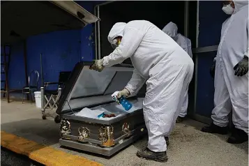  ?? Associated Press ?? ■ A worker wearing protective gear sprays disinfecta­nt solution inside the coffin of a person who died from suspected COVID-19, as the body arrives July 27 at the crematoriu­m at Xilotepec Cemetery in Xochimilco, Mexico City.