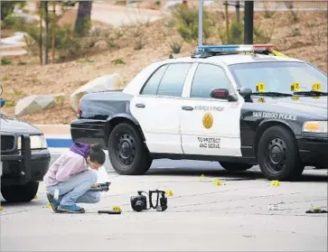  ?? Photograph­s by Howard Lipin San Diego Union-Tribune ?? SAN DIEGO POLICE examine what appears to be a gun on the ground at the scene of the shooting Saturday outside Torrey Pines High School. Investigat­ors say it is too early to label the boy’s death a “suicide by cop.”