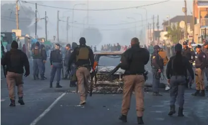  ?? Photograph: Esa Alexander/Reuters ?? Police stand near a burnt-out vehicle in Nyanga, Cape Town during the strike, 7 August 2023. Five people have been killed in the violence, police said.