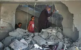  ?? GETTY-AFP ?? A Palestinia­n woman and children step through rubble Saturday in a house hit by an Israeli airstrike in Rafah, in the Gaza Strip. At least nine people died, authoritie­s said.