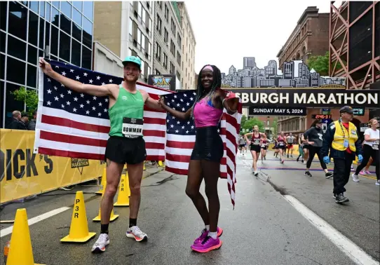  ?? Lucy Schaly/Post-Gazette ?? Pittsburgh Marathon men’s elite winner Andrew Bowman and women’s elite winner Jane Bereikis hold American flags Sunday on the Boulevard of the Allies, Downtown.