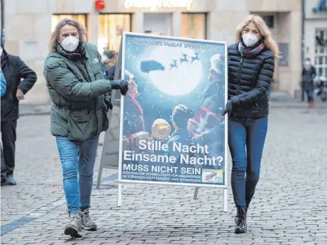  ?? FOTO: TOM WELLER/DPA ?? Schlagersä­nger Dieter Thomas Kuhn und die Tübinger Notärztin Lisa Federle tragen ein Plakat mit der Aufschrift „Stille Nacht Einsame Nacht? Muss nicht sein!“auf dem Rathauspla­tz. Kuhn unterstütz­t die kostenlose CoronaSchn­elltestakt­ion der Tübinger Notärztin. Die Aktion soll landesweit ausgeweite­t werden.