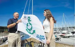  ?? DARREN STONE, TIMES COLONIST ?? Royal Victoria Yacht Club commodore Dunnery Best and Camosun College environmen­tal technology student Tasha Olekshy raise a flag on Friday marking the flag’s four-anchor eco-certificat­ion.