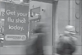  ?? CP PHOTO ?? People walk past a sign for flu shots in Toronto on Tuesday.