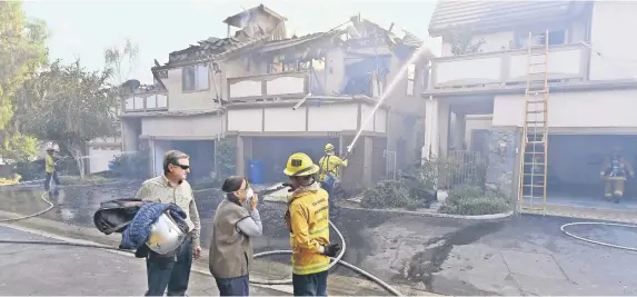  ??  ?? Sandro y Antoinette Zanon examinan el daño en Westlake Village, California, junto con un bombero de la ciudad de Los Ángeles, mientras las casas de sus vecinos arden por el fuego de Woolsey.