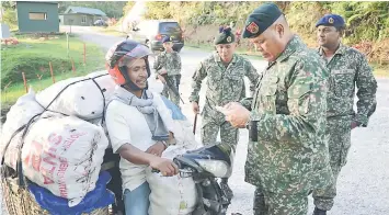  ??  ?? Mundaw checking the identifica­tion of a trader carrying his goods at Serikin, Bau on Monday. – Photo courtesy of the Malaysian Army