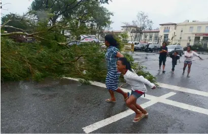  ?? Reuters ?? Residents rush to safety past a fallen tree during strong winds brought by Typhoon Haiyan in central Philippine­s. —