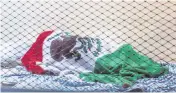  ?? PEDRO PORTAL pportal@miamiheral­d.com ?? A person wrapped in a Mexican flag sleeps on the floor of a strip mall located next to the Home Depot parking lot in Hialeah, early in the morning on Feb. 14.