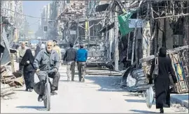  ?? Syrian Arab News Agency ?? PEOPLE pass damaged buildings in Duma after the Syrian army retook the city.