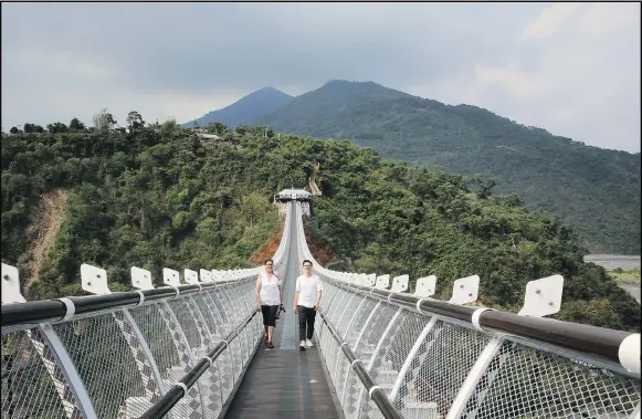  ?? DAVID CONACHY ?? StarPhoeni­x reporter Betty Ann Adam and university student Auvunni Abaliusu, of the Rukai tribe, cross the Glass Suspension Bridge, with its totemic Hundred Pacer Snake suspender braces, which spans the Ailiao River valley in southern Taiwan.