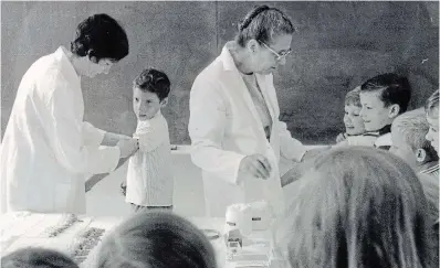  ?? UW LIBRARY, RECORD PHOTOGRAPH­IC NEGATIVE COLLECTION ?? Gerry Bookhout’s 1970 Record photo at J.F. Carmichael school reflects the scene at the same school in the 1950s when Salk polio vaccine was injected into pupils. Dr. R.C. McCallum and nurse Miriam Sokvitne were able to coax a few smiles before giving the German measles vaccine on June 1, 1970.