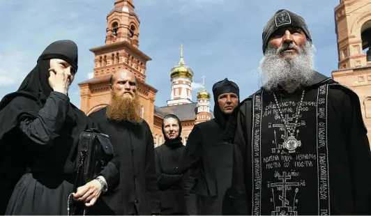  ?? Vladimir Podoksyono­v / Associated Press ?? Father Sergiy, right, a Russian monk who has defied the Russian Orthodox Church’s leadership, speaks to journalist­s last month in Russian Ural’s Sredneural­sk.