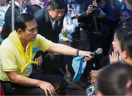  ?? — Reuters ?? Giving a voice: Prayuth holding a microphone as he listens to family members near the Tham Luang cave complex in the northern province of Chiang Rai, Thailand.