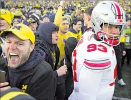  ?? David Dermer Associated Press ?? MICHIGAN FANS celebrate as Ohio State defensive tackle Hero Kanu tries to navigate his way off the field after the Buckeyes’ 30-24 loss to the Wolverines.