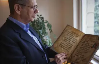  ?? DAN BALILTY/THE ASSOCIATED PRESS ?? Eli Barzilai holds a copy of the Birds’ Head Haggadah in Jerusalem. Barzilai and his cousins, the grandchild­ren of one of the earliest Jewish victims of the Nazis, are laying claim to a jewel of Israel’s leading museum.