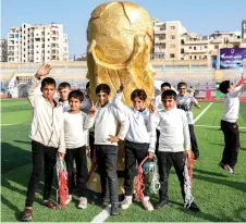  ?? — AFP photo ?? Youths pose by a mockup of the FIFA World Cup trophy on the pitch during the opening ceremony of the ‘Camps World Cup’ at the newly-reopened Idlib Municipal Stadium in the rebel-held northweste­rn Syrian city.