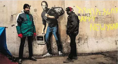  ?? AFP ?? Two men stand next to a street art graffiti by elusive British artist Banksy representi­ng Steve Jobs, founder and late CEO of Apple, at the migrant camp known as the ‘Jungle’ in Calais, northern France, on Saturday.