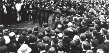  ?? Library of Ireland Photo National ?? Members of the Irish Volunteers fire a volley of shots over the grave of Tomás Ashe at his funeral in Glasnevin Cemetery.