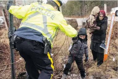  ?? RYAN REMIORZ / THE CANADIAN PRESS FILES ?? An RCMP officer helps asylum seekers, who said they were from Turkey, cross the border from New York state into Canada last year at Hemmingfor­d, Que.