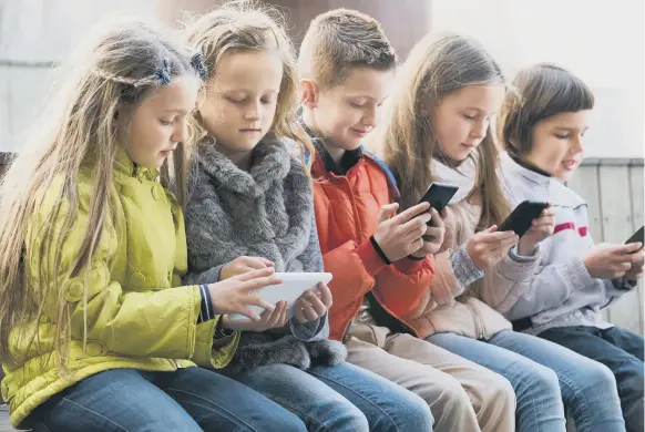  ??  ?? A familiar sight for many parents - children absorbed on their smartphone­s and tablets.