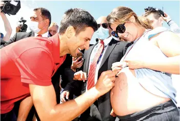  ?? - AFP photo ?? Djokovic (left) signs on a pregnant woman Vanessa Kezerle’s belly during a photo shoot for his winning the Norman Brookes Challenge Cup trophy.