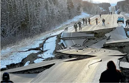  ?? AP ?? People walk along Vine Road which was damaged in an earthquake in Wasilla, Alaska.