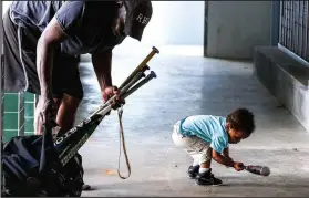  ?? Arkansas Democrat-Gazette/MITCHELL PE MASILUN ?? Tony Dunnick gets some help with his bats from his son David Wayne Reynolds Dunnick, 15 months, during practice at Lamar Porter Field in Little Rock.