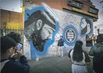  ?? Allen J. Schaben Los Angeles Times ?? VISITORS TAKE photos and video next to murals of rapper Nipsey Hussle at the strip mall he owned in South Los Angeles. An aspiring rapper from the neighborho­od he grew up in is accused of killing him.