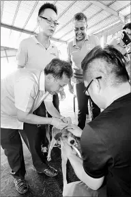  ??  ?? Dr Sim giving a vaccinatio­n jab to a dog. Watching him are Rebecca (right) and SUPP Youth Central publicity secretary Milton Foo (standing left).