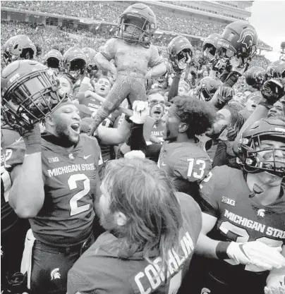  ?? JAKE MAY/THE FLINT JOURNAL ?? Michigan State players celebrate with the Paul Bunyan trophy after Saturday’s win over Michigan.