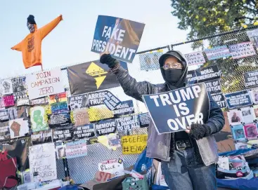  ?? JOHN MINCHILLO/AP ?? A demonstrat­or stands in front of a fence covered in protest signs Nov. 2 on the north side of the White House. Voters went to the polls the following day to choose between giving President Trump a second term in office or replacing him with former Vice President Joe Biden. The Electoral College this week affirmed Biden’s victory and he will be inaugurate­d Jan. 20.