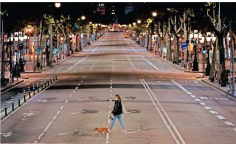  ?? FOTO: MORENATTI/DPA ?? Eine Spanierin trägt Maske, als sie mit ihrem Hund eine leere Straße in Barcelona überquert, nachdem eine Ausgangssp­erre verhängt worden ist.