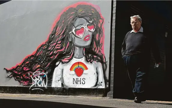  ?? FOTO REUTERS ?? Miluji NHS. Muž v britském městě Redcar prochází kolem graffiti vyjadřujíc­ího podporu britským zdravotník­ům odkazem na zkratku tamního zdravotníh­o systému (NHS).