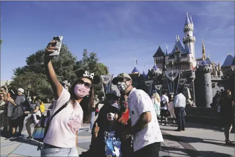  ?? AP PHOTO/JAE HONG ?? A FAMILY TAKES A PHOTO IN FRONT OF SLEEPING BEAUTY’S CASTLE at Disneyland in Anaheim, Calif., on Friday. The iconic theme park in Southern California that was closed under the state’s strict virus rules swung open its gates Friday and some visitors came in cheering and screaming with happiness.