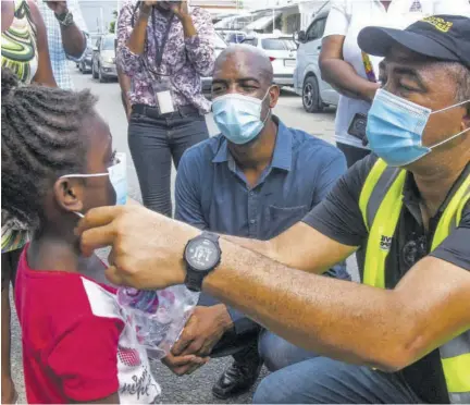  ?? (Photo: Karl Mclarty) ?? Minister of Health and Wellness Dr Christophe­r Tufton places a mask on Arrianna Shelton during a visit to Waterford, St Catherine, recently.