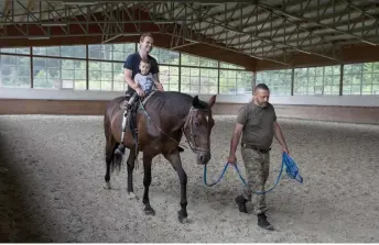  ?? ?? Vasyl Irkha leads Serheii, 26, during a therapeuti­c horseback riding lesson as Egor, 2, shares the saddle with his father on July 31.