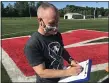  ?? JOHN KAMPF — THE NEWS-HERALD ?? Ken Skilton, new girls soccer coach at Mentor, looks over his roster June 8on the first day of workouts at the school.